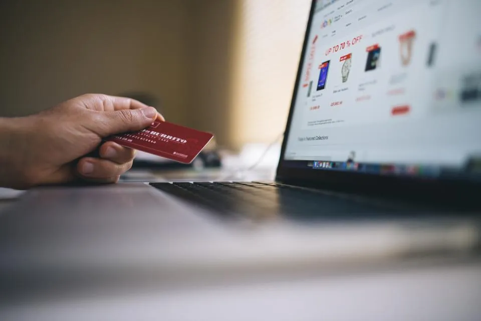 Tangan memegang kartu pembayaran di depan laptop yang menampilkan toko online
